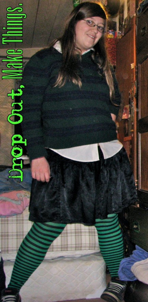 A picture of brown haired girl wearing a white collared shirt with a forest green and navy blue striped sweater over it; a gathered black skirt made from shiny fabric, and green and black striped tights